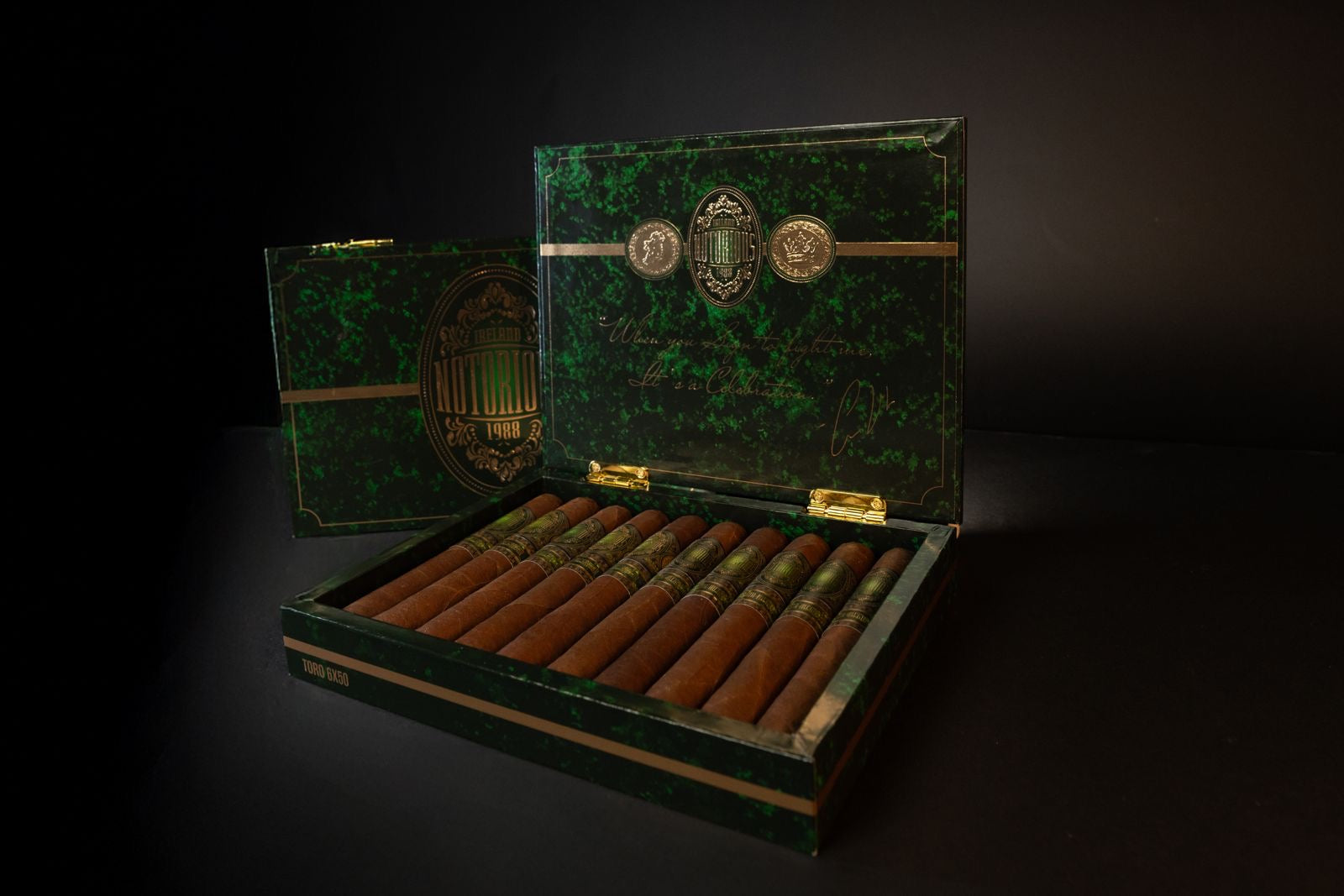 Open box of Notorious Cigars featuring ten premium cigars with ornate green bands, displayed in a luxurious green and gold humidor.